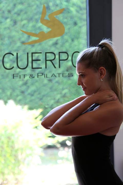 Allieva con le mani dietro la nuca davanti al logo Cuerpo Fit & Pilates