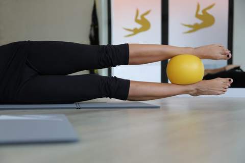 Esercizio di Pilates con una palla gialla tra le caviglie